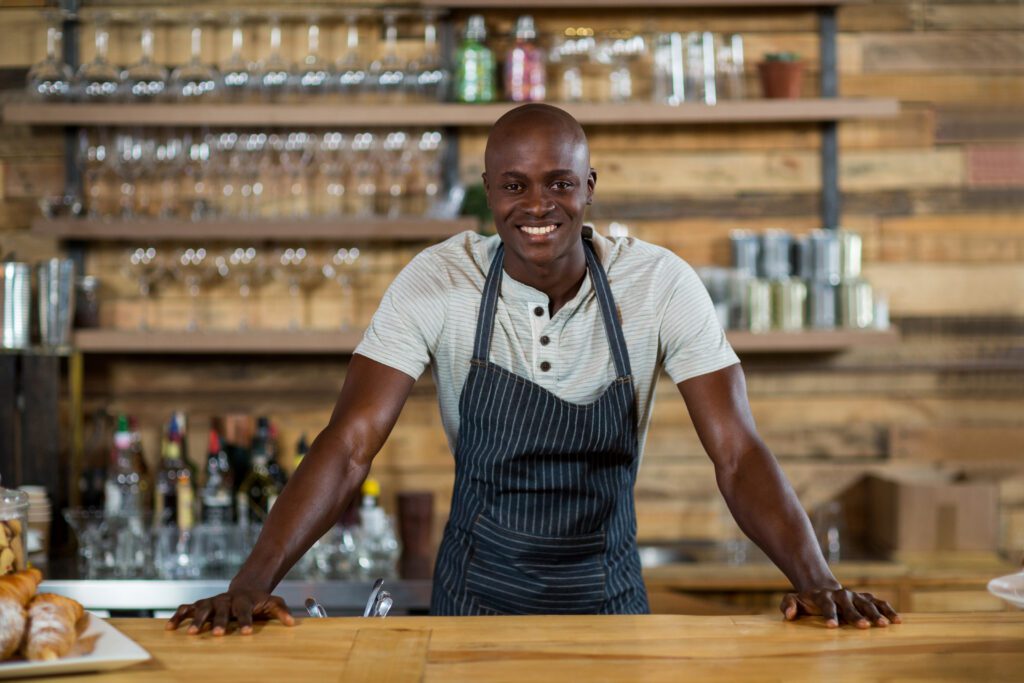 Portrait of smiling waiter standing at counter in cafe